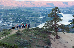 people standing on top of saddle rock looking down at the river at sunset